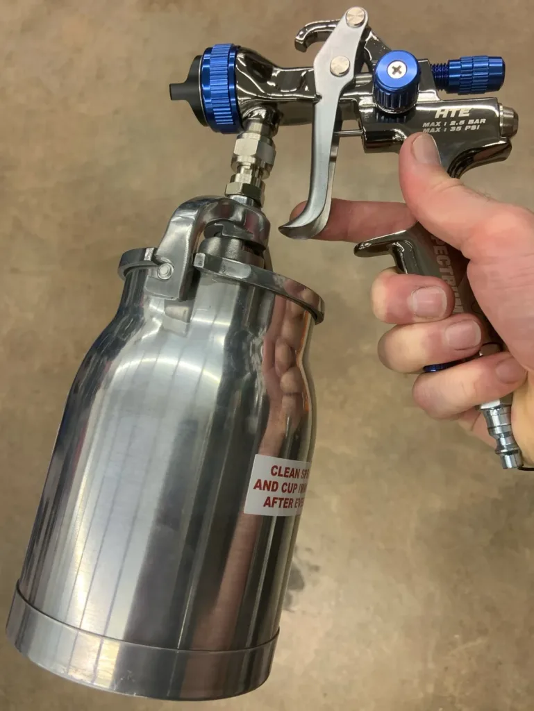 Pistola de pintura com caneca de alumínio, segurada com a mão